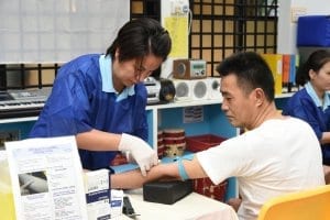 Woman doing a vein puncture on a man during a wellness biometric screening event.