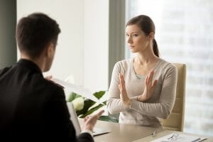 Woman with her hands crossed showing unacceptance of paper being handed by a person in a black suit.