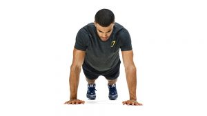 Man on the floor in a grey shirt and black pants going a pushup.