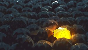 A single bright glowing umbrella in a sea of black umbrellas during a rain storm.