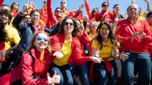 Group of people at a sports game cheering for a yellow and red team.