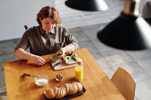 Woman in a wheelchair sitting at a table cutting and eating an avocado.