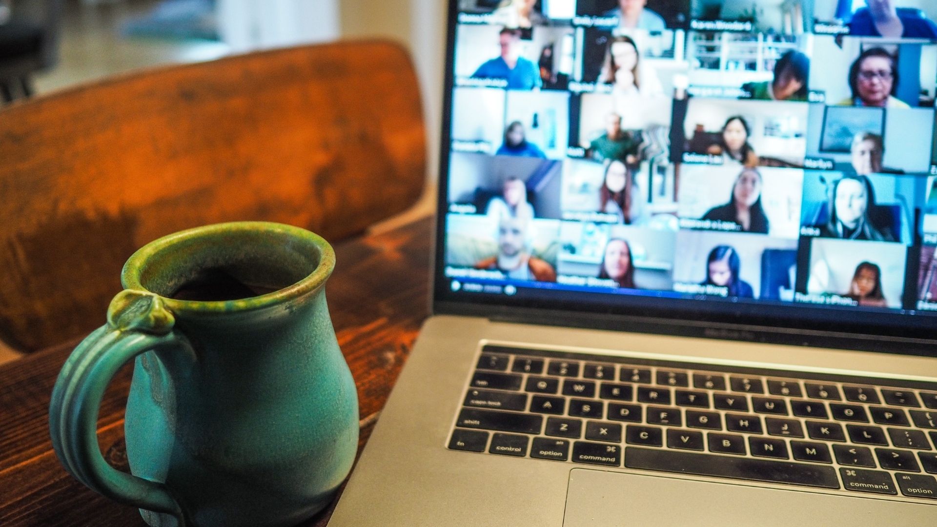 Computer screen showing a video call with many different attendees and a mug on the table.