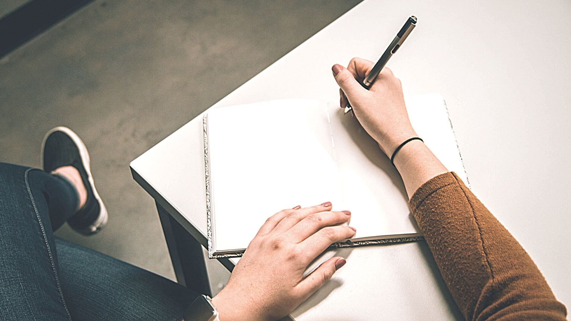 Close up of a woman in a brown sweater holding a pen beginning to write in a journal. Questions to ask while evaluating a wellness program