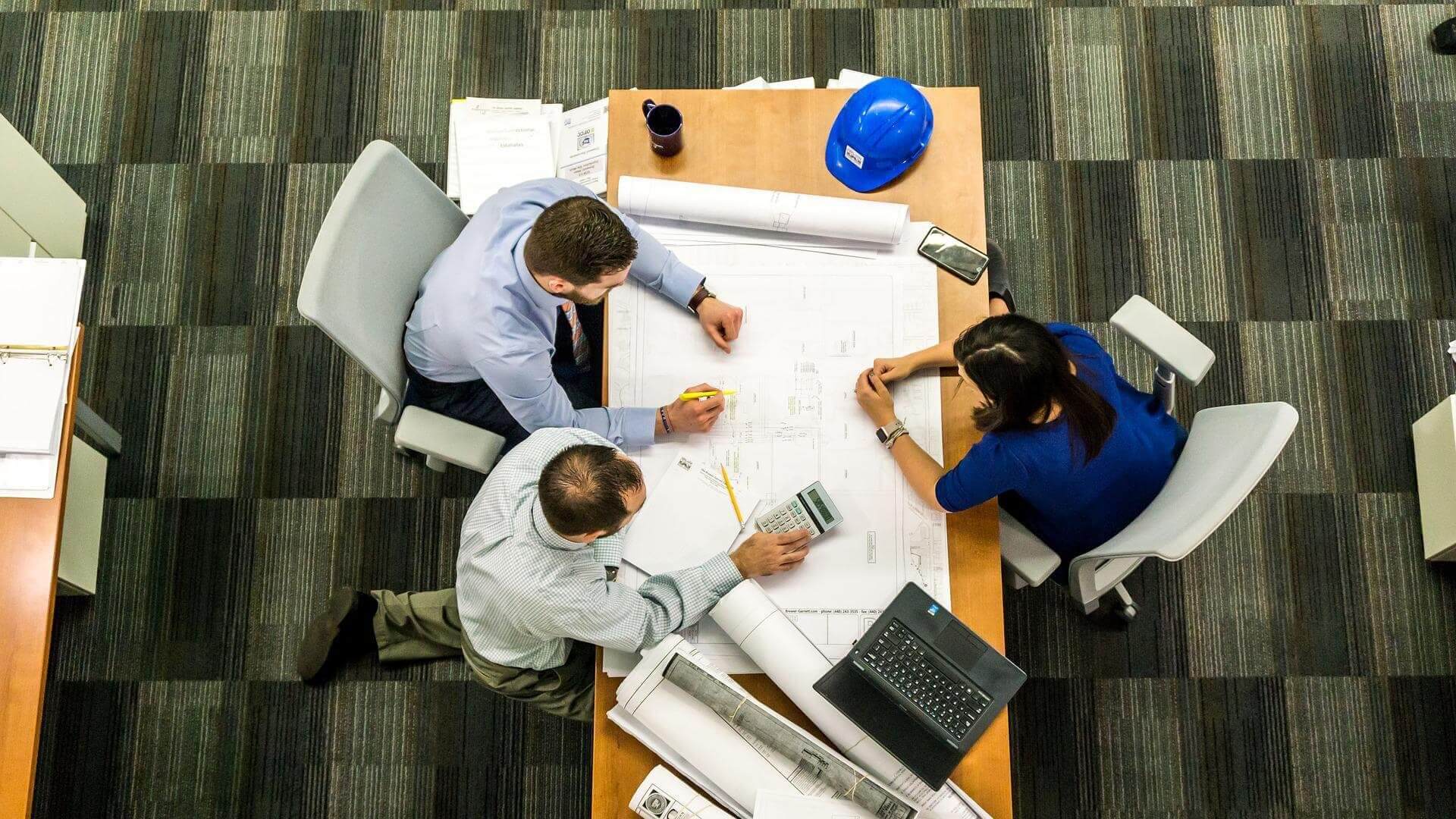 Overhead view of three people marking a building schematic displayed on a large table.