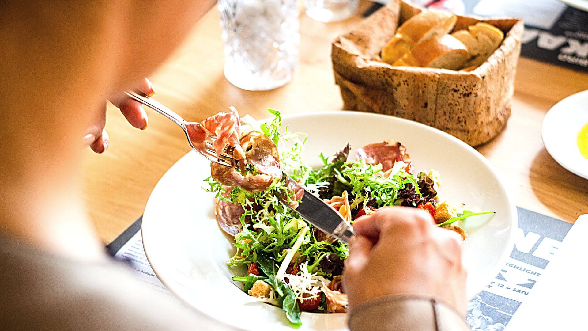 Closeup of a person eating a fresh salad with a basket of fresh bread on the table.