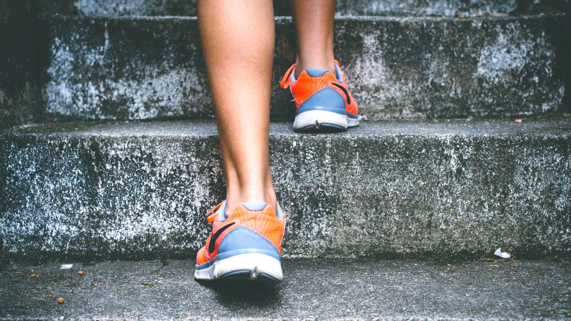 Closeup of person in blue and orange shoes climbiing up stairs. Easy ideas for increased fitness in the workplace
