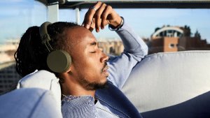 Man sitting on an outdoor couch on a rooftop listening to headphone with eyes closed.