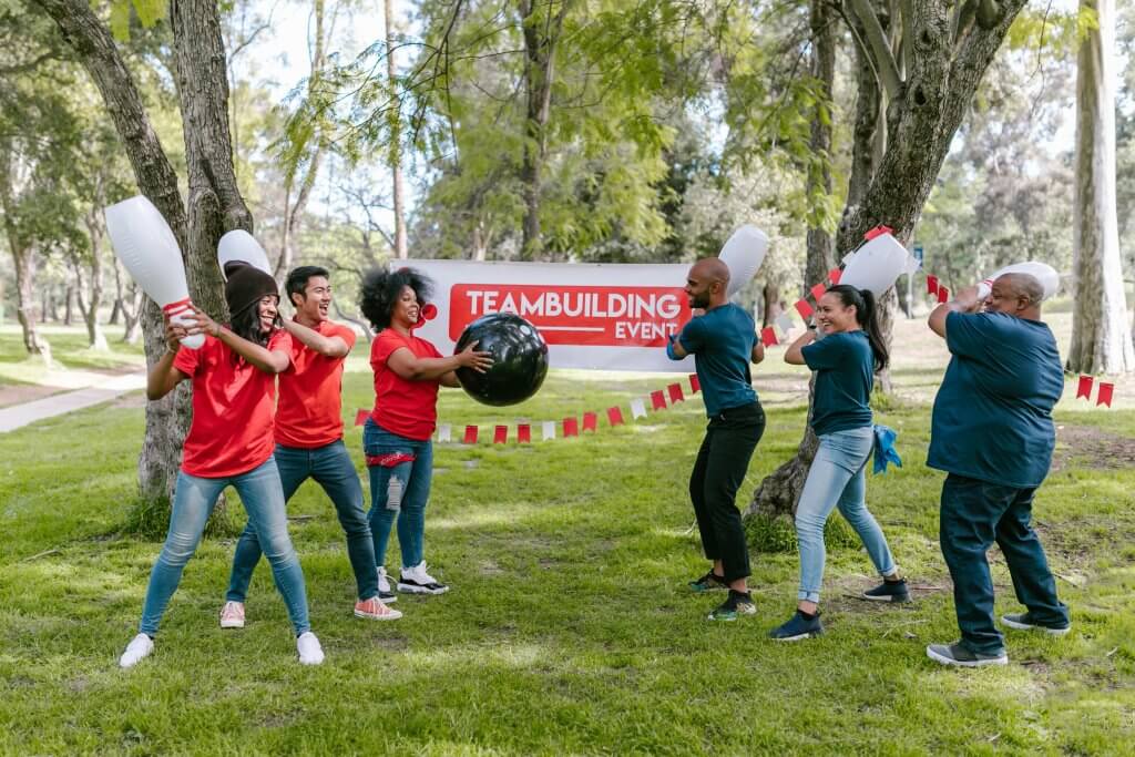 Two small groups of workers engaging in an interactive bowling ball game outdoors at a team building event.